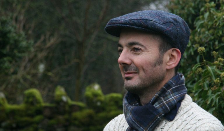 Man wearing Harris Tweed flat cap, lambswool scarf and Aran Jumper